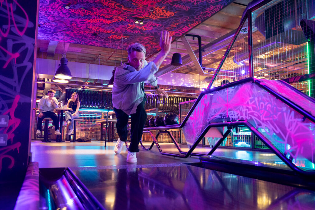 Man in a white jacket bowling a ball down a lane